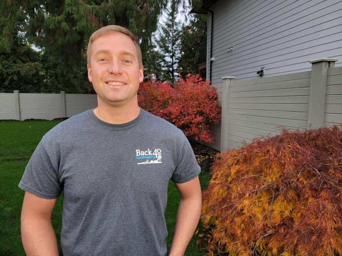 Sam Maerz, co-owner of Back 40 Landscaping in Abbotsford, BC, standing in a landscaped backyard with autumn foliage