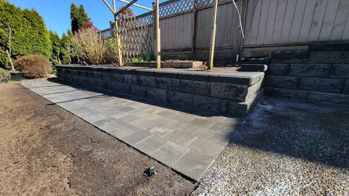 Close-up of paved pathway and stone retaining wall in landscaped garden by Back 40 Landscaping in Burnaby, BC