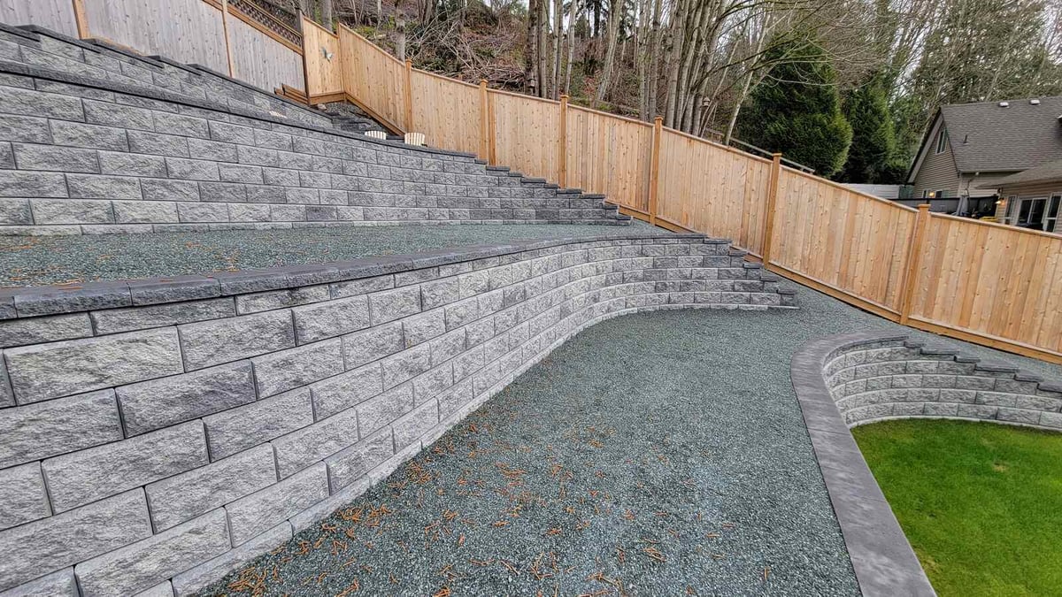 Side view of a tiered retaining wall with wooden fence in a Langley, BC project by Back 40 Landscaping