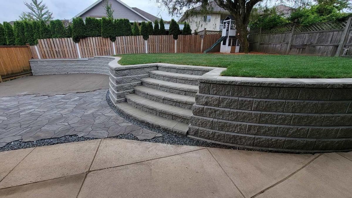 Stone steps and curved retaining wall bordering a landscaped lawn by Back 40 Landscaping in Mission, BC